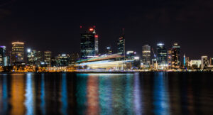 A ferry crossing the Swan River with the illuminated Perth skyline glowing against the night sky.